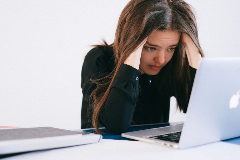 Junge Frau schaut verzweifelt auf Laptop mit den Händen am Kopf