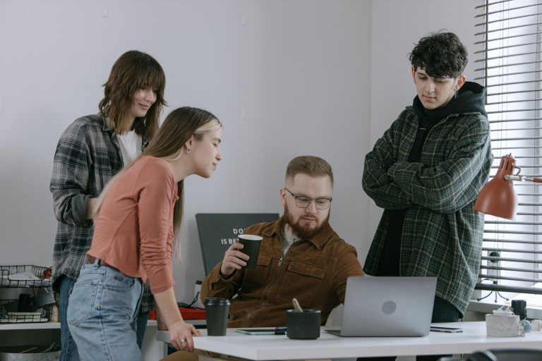 Startup Team aus vier jungen Leuten schaut zusammen auf Laptop
