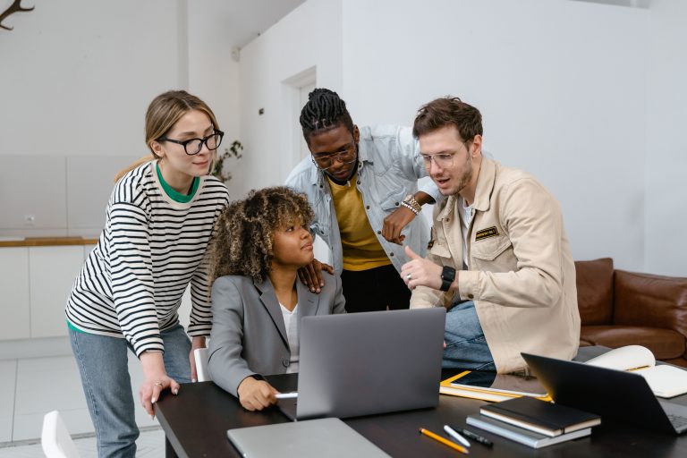 Junges Startup-Team sitzt um Laptop, Gründer mit Brille erklärt etwas