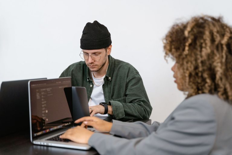 Frau und traurig wirkender Mann sitzen an Laptop und arbeiten