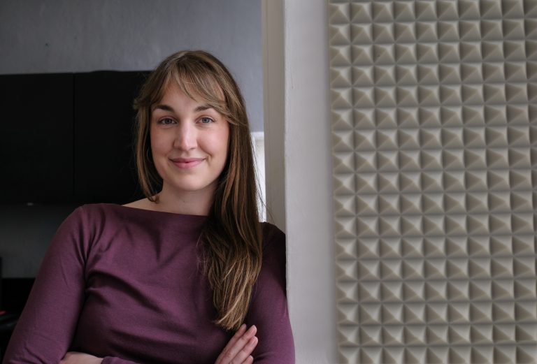 Tess Höke, Business Coach für Gründer und Gründerinnen, lehnt leicht lächelnd an einer Wand
